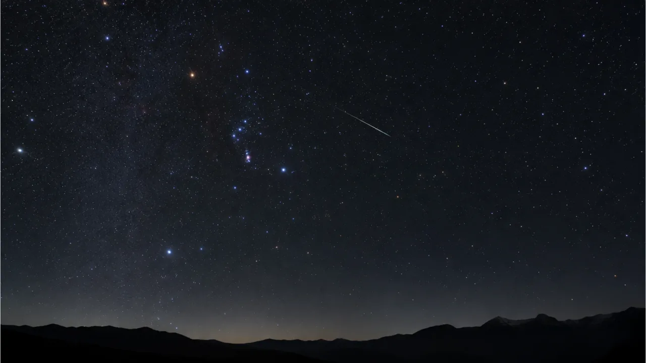 A dark night sky with a meteor streaking near the constellation Orion
